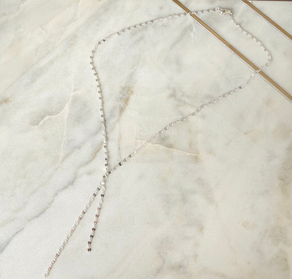 Silver lariat necklace on a marble surface
