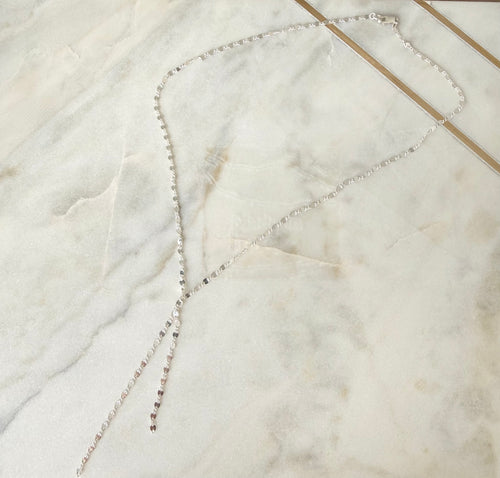 Silver lariat necklace on a marble surface