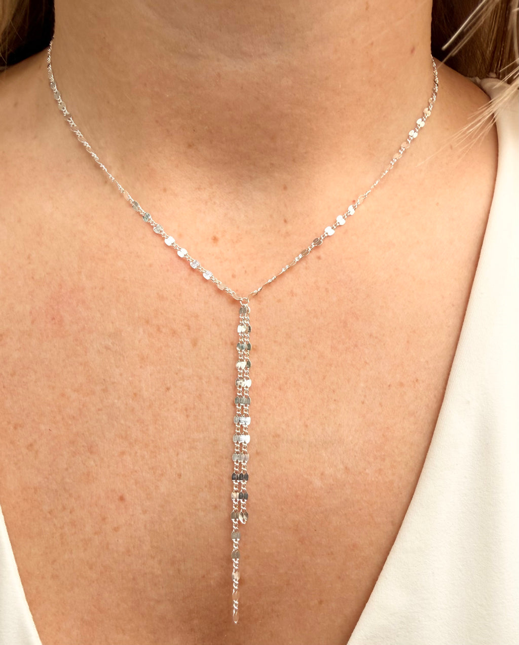 Silver lariat necklace on a person wearing a white top