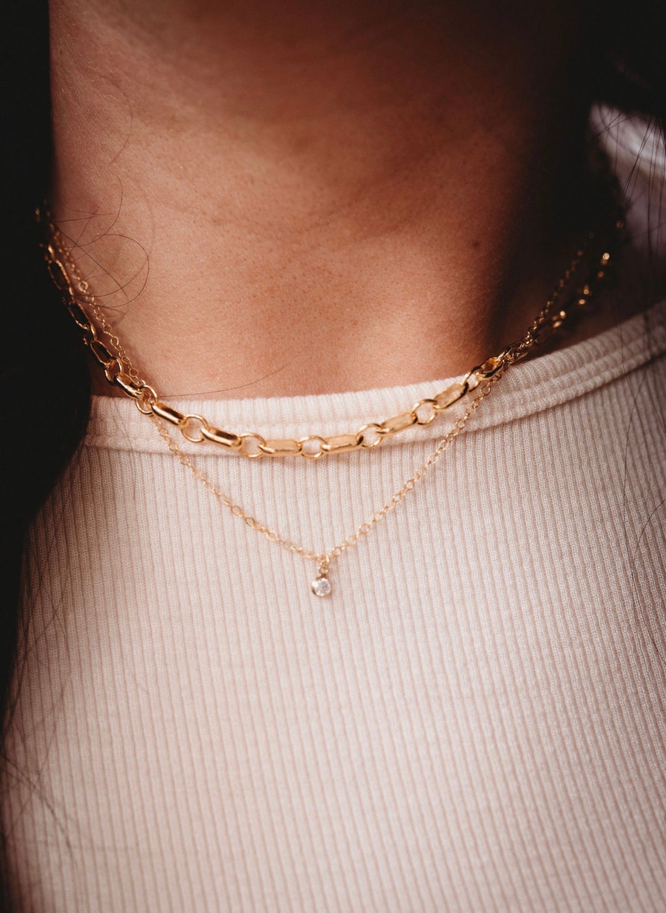 2 Gold chain necklace on a person wearing a white top.