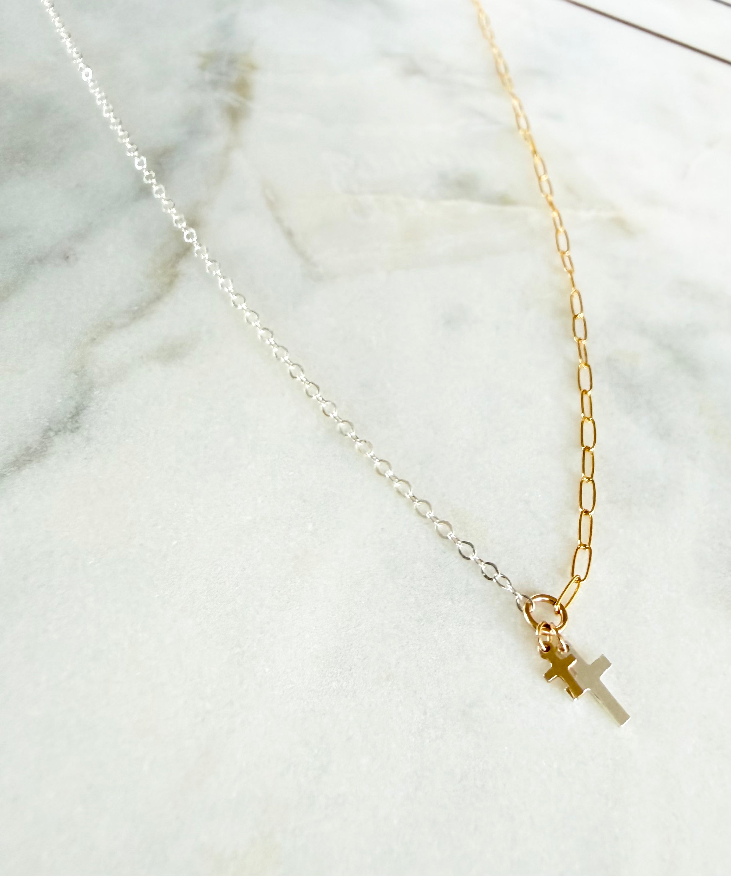 Two gold necklaces with cross pendants on a marble surface