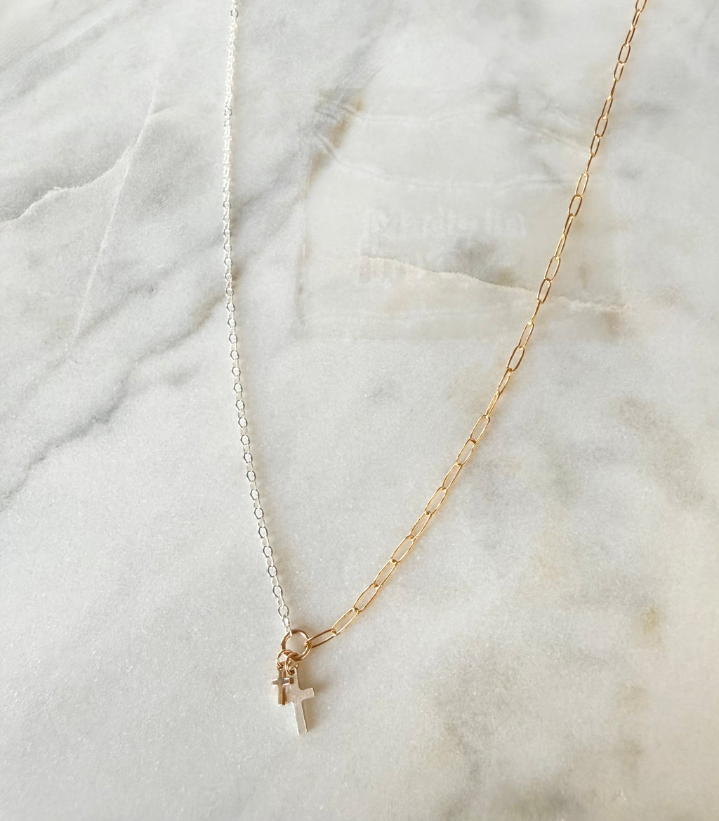 Gold and silver necklace with a cross pendant on a marble surface