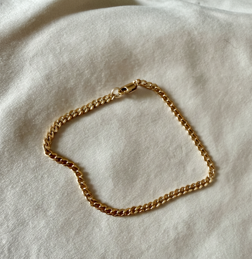 Gold chain bracelet on a light beige fabric background