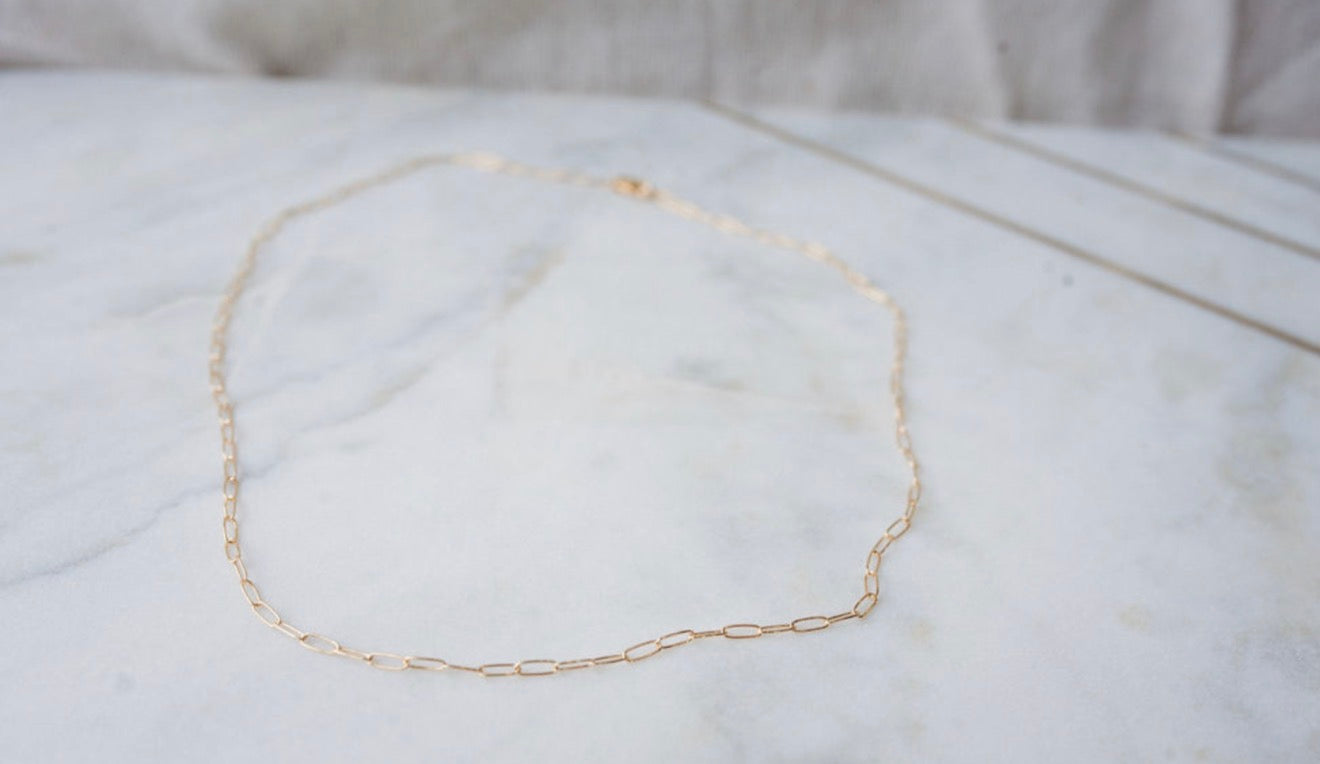 Gold paper hip chain necklace on a textured white surface
