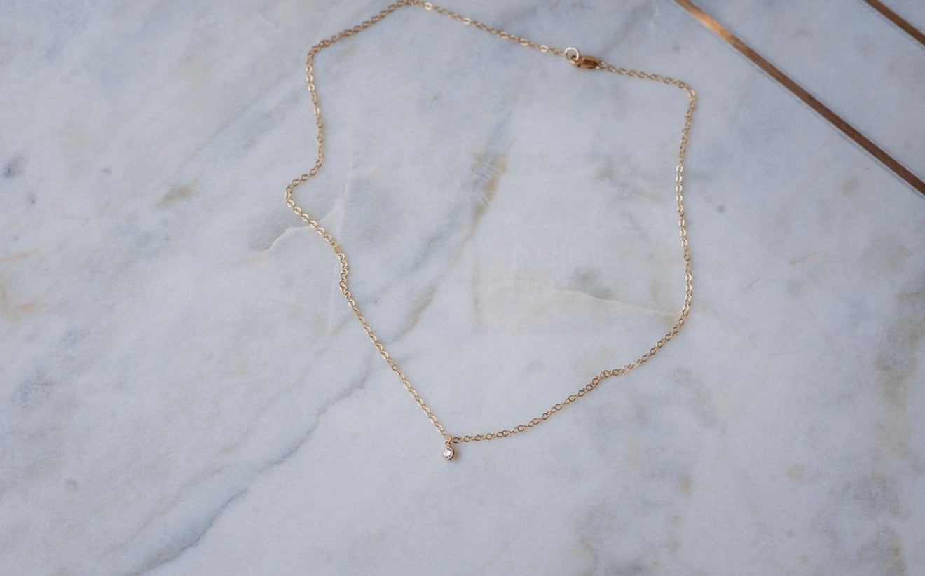 Gold necklace with diamond pendant on a marble surface