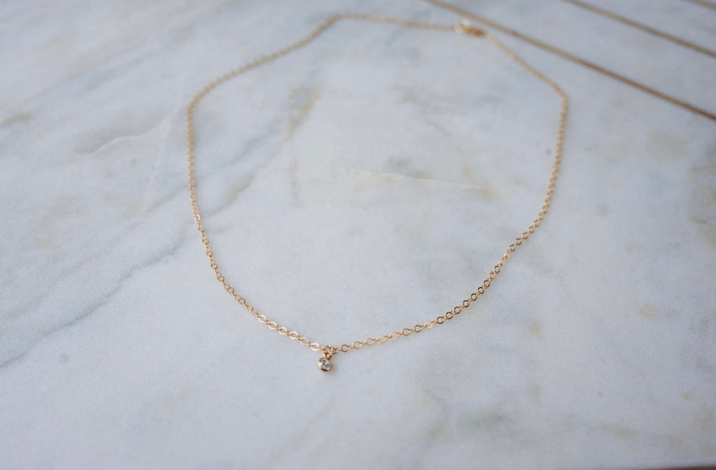 Gold necklace with diamond pendant on a marble surface