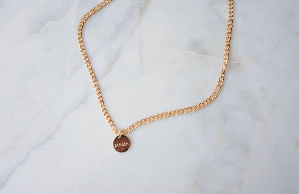 Thick Gold chain necklace with a  mama round tag on a marble surface