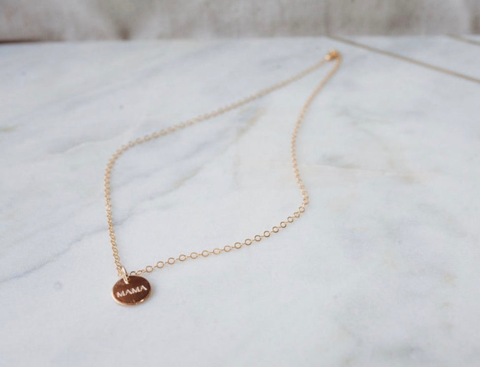 Gold necklace with a 'MAMA' pendant on a marble surface