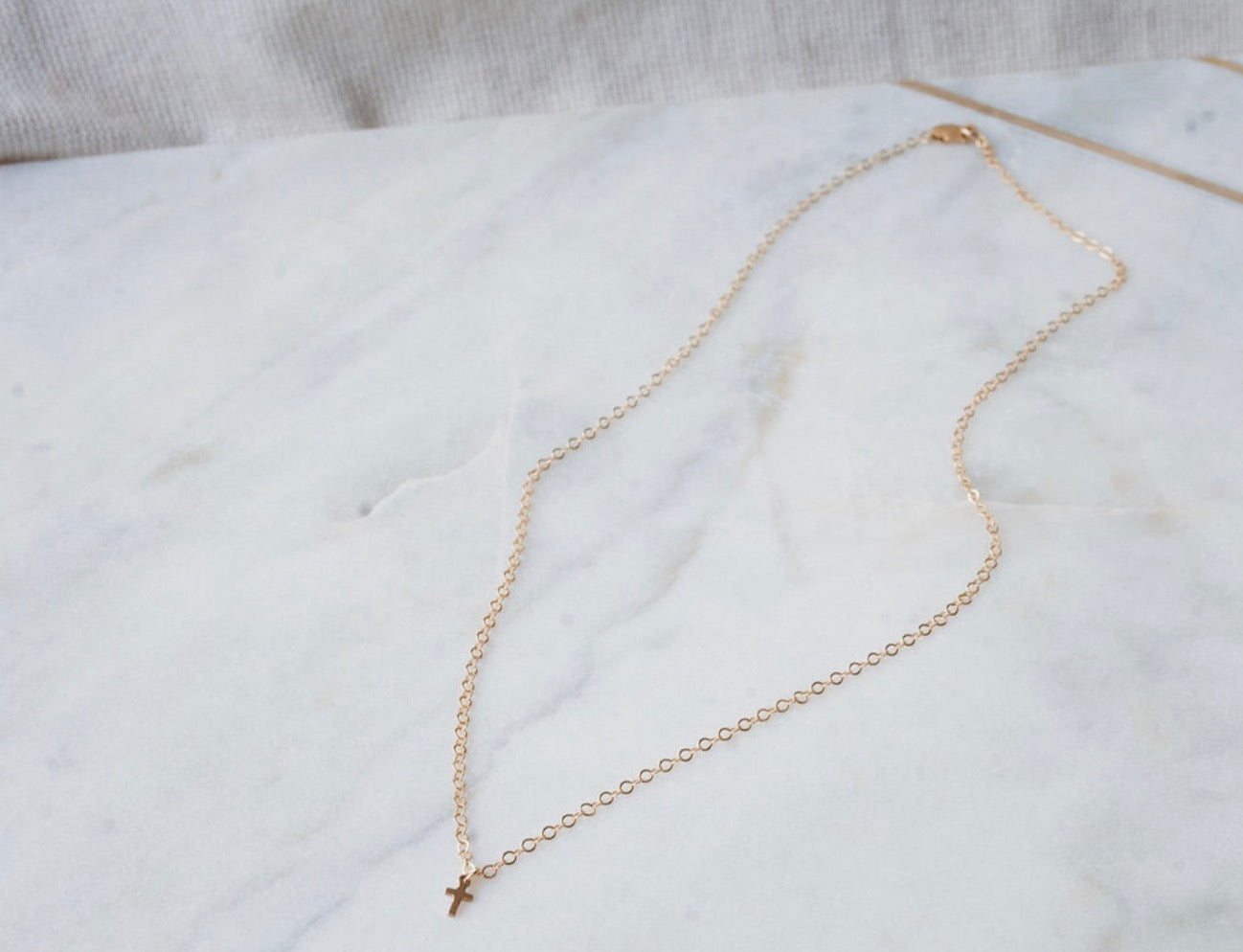 Gold necklace with a small cross pendant on a white marble surface