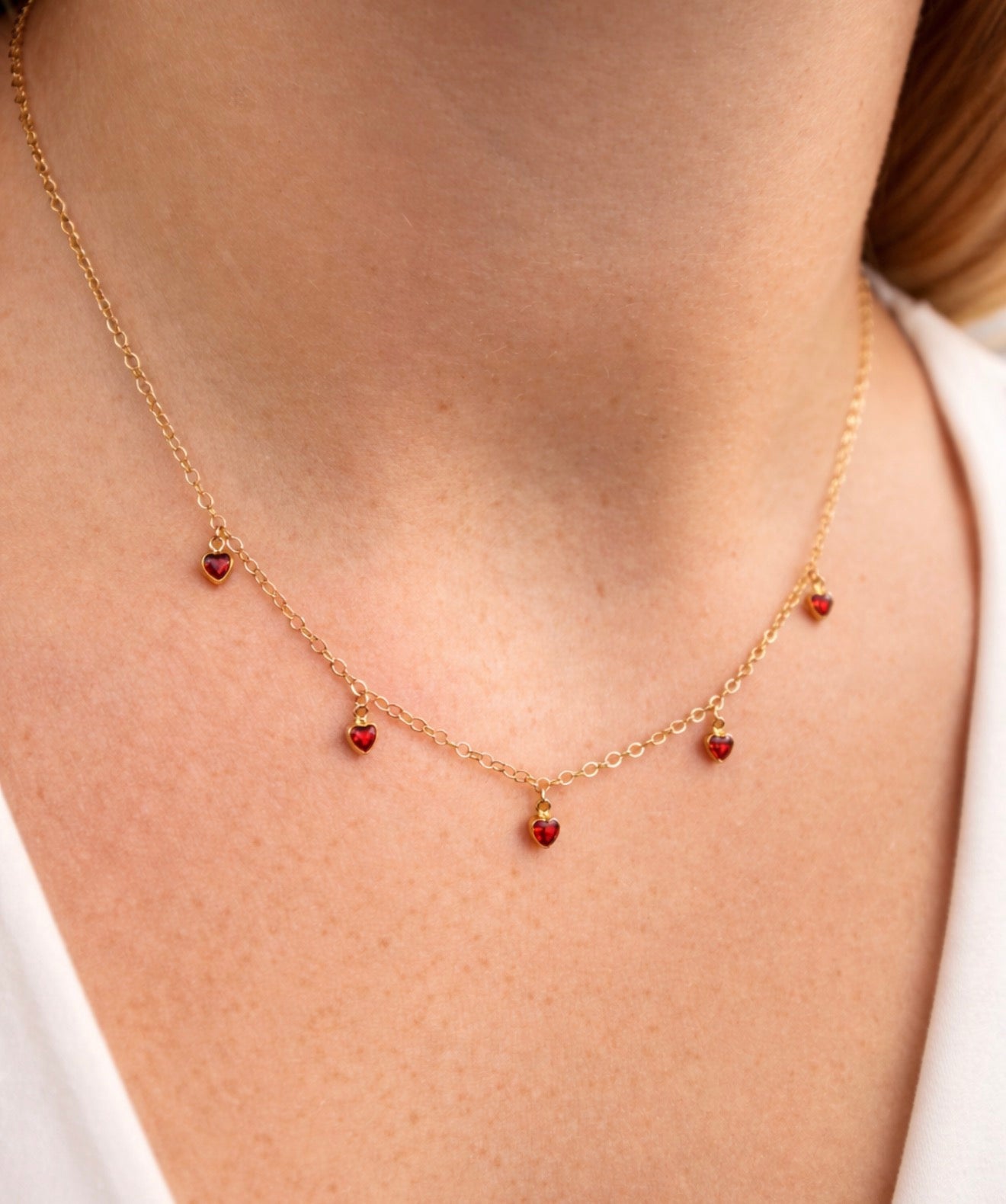 Gold necklace with red heart charms worn by a person