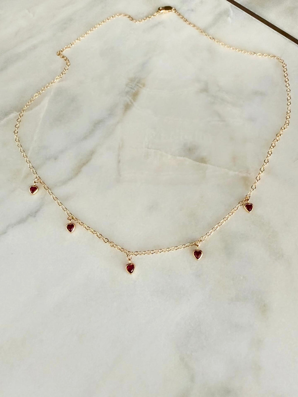 Gold necklace with 5 heart-shaped pendants on a marble surface