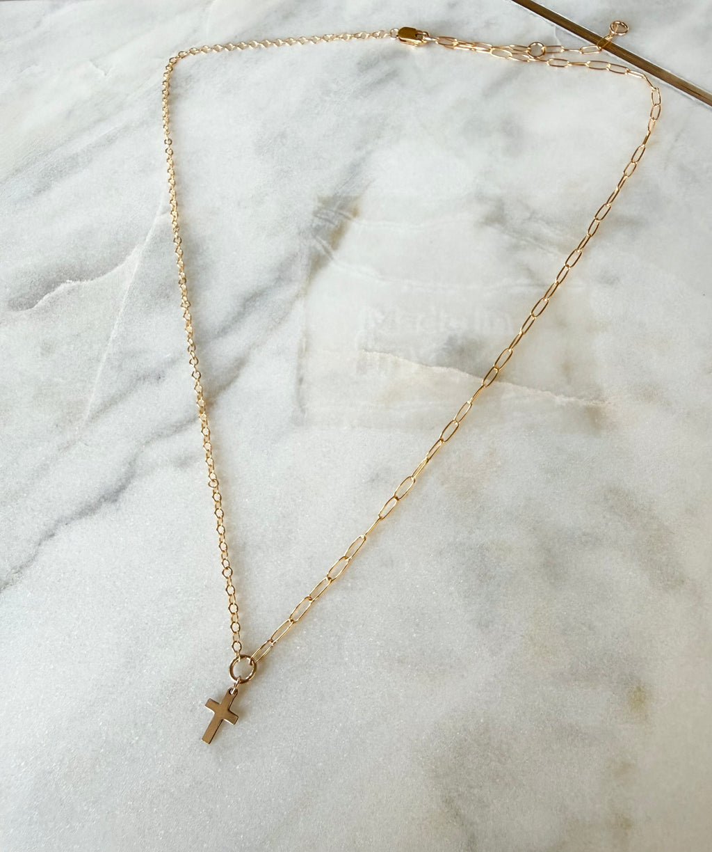 Gold necklace with a cross pendant on a marble surface