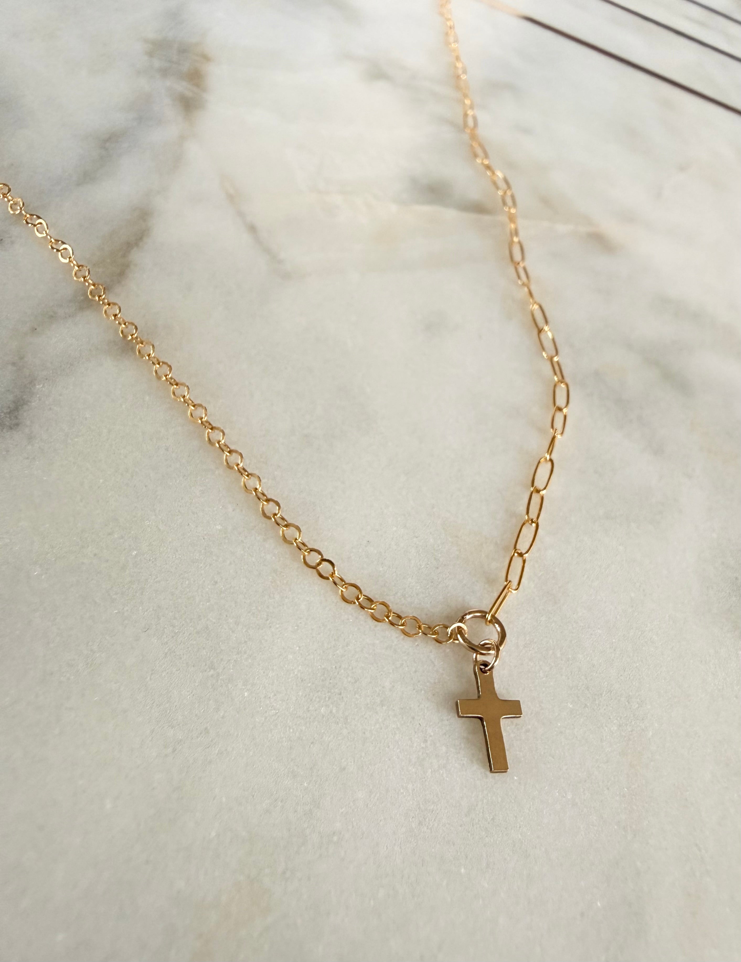 Gold necklace with a cross pendant on a marble surface