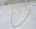 Gold chain necklace with a pearl on a white fabric background