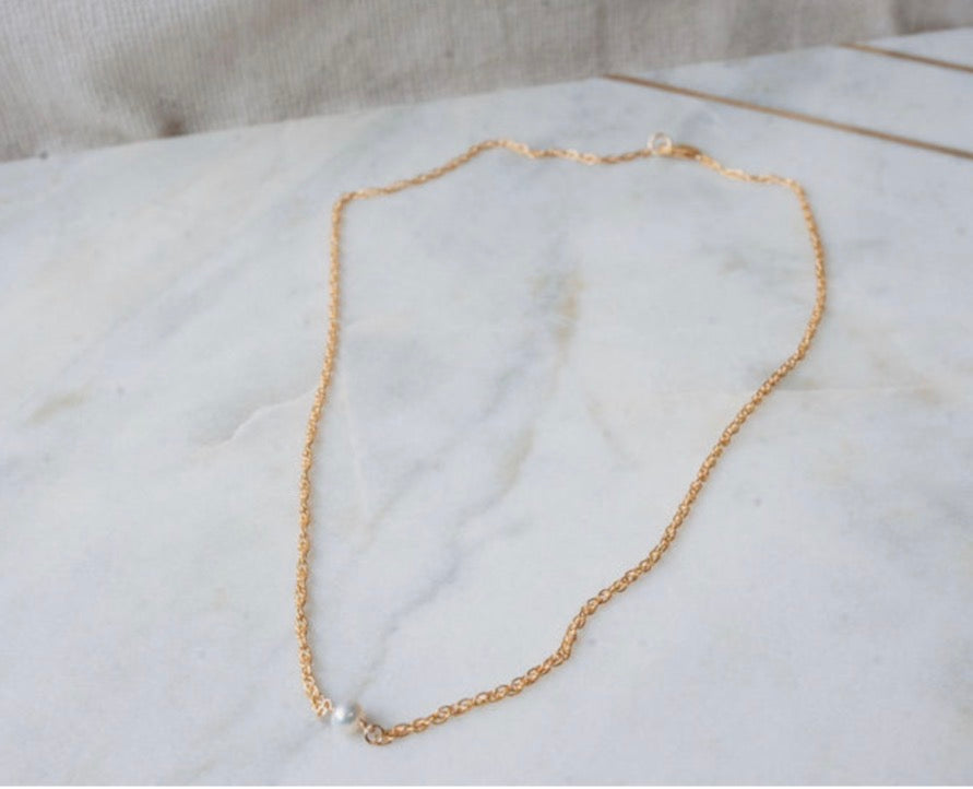 Gold chain necklace with a pearl on a white fabric background