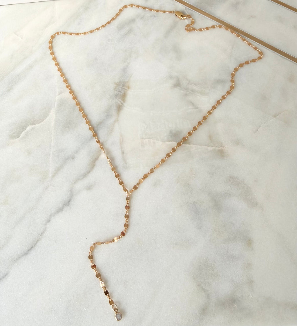 Gold lariat necklace with small stone on it. on a marble surface