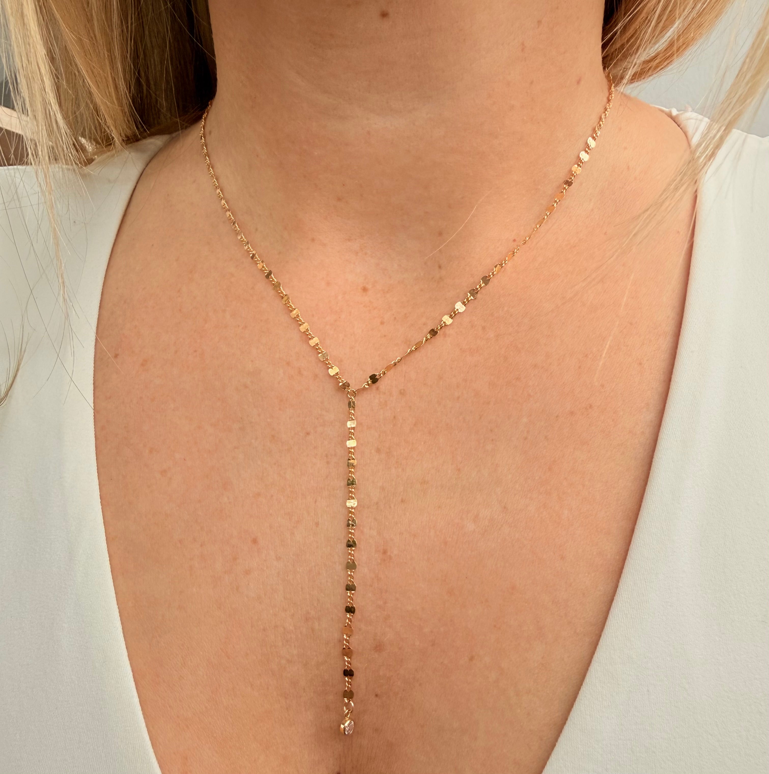 Gold lariat necklace with small stone, on a person wearing a white top