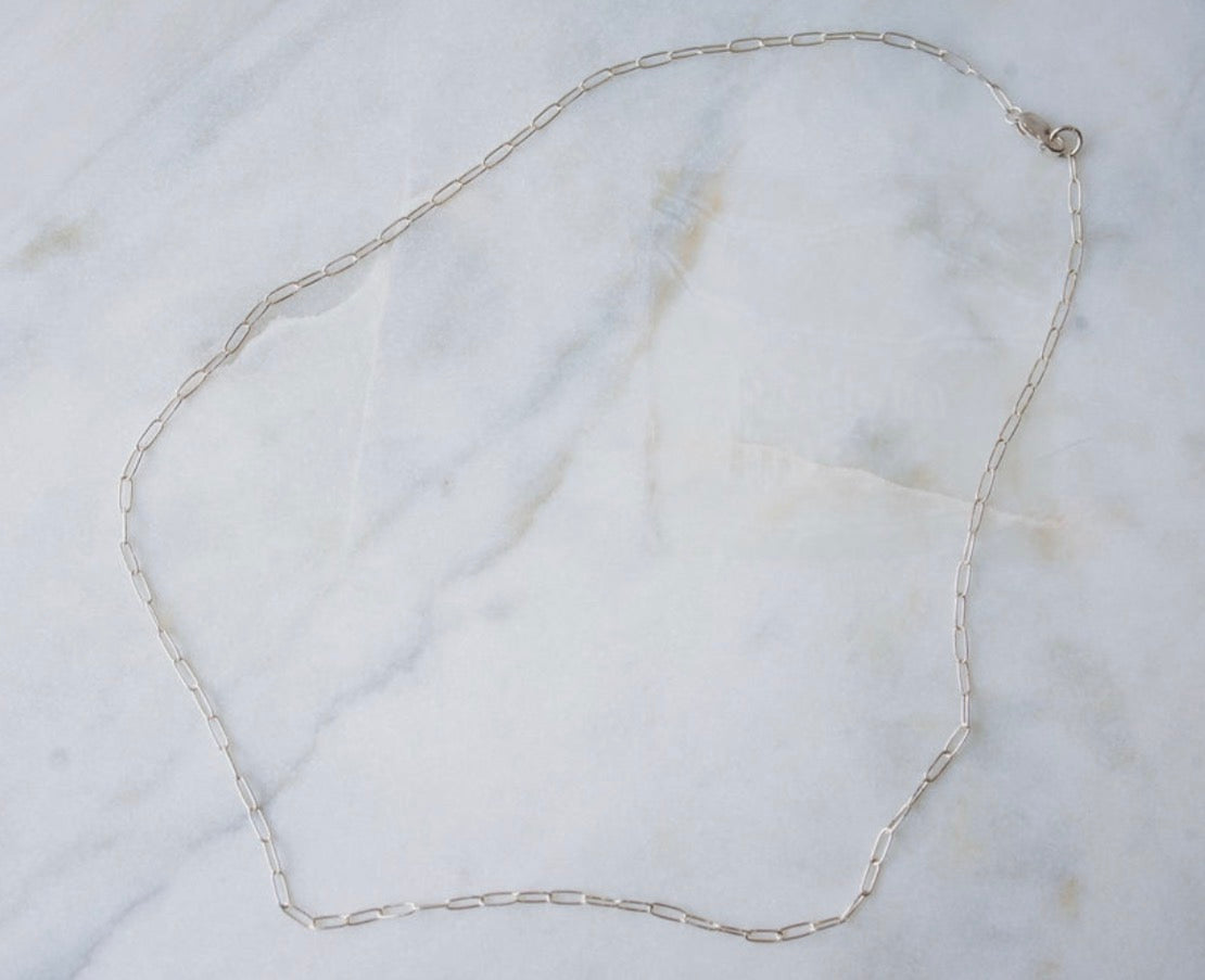 Silver paperclip chain necklace on a marble surface
