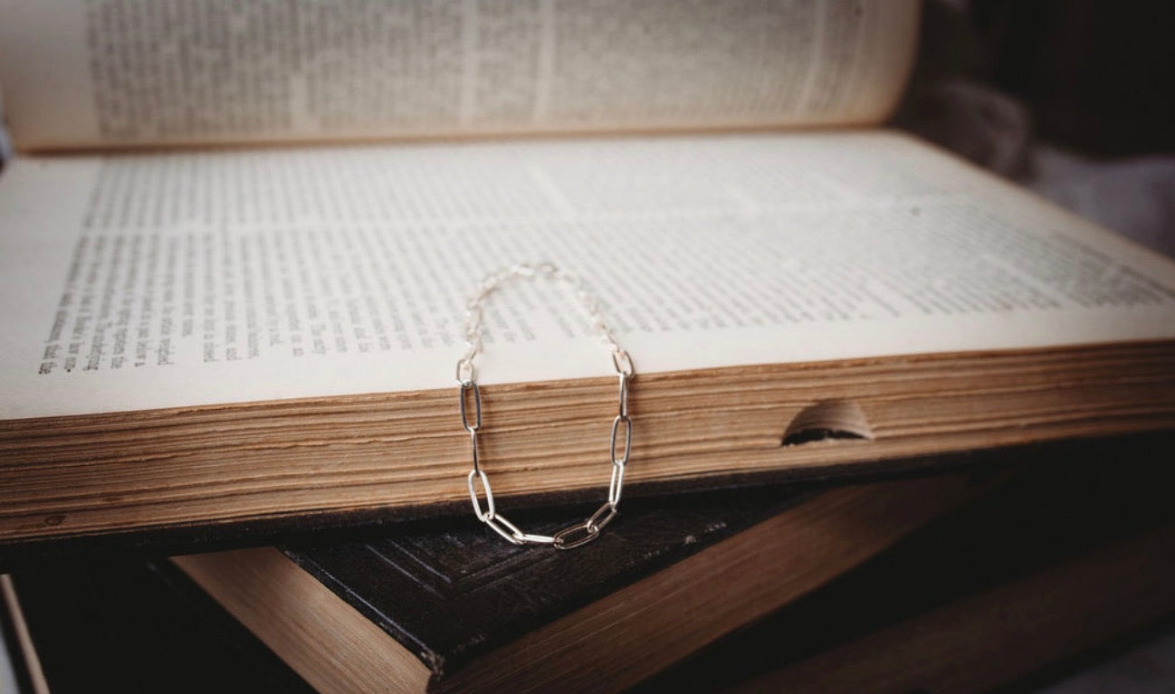 Thick silver paperclip bracelet draped over an open book