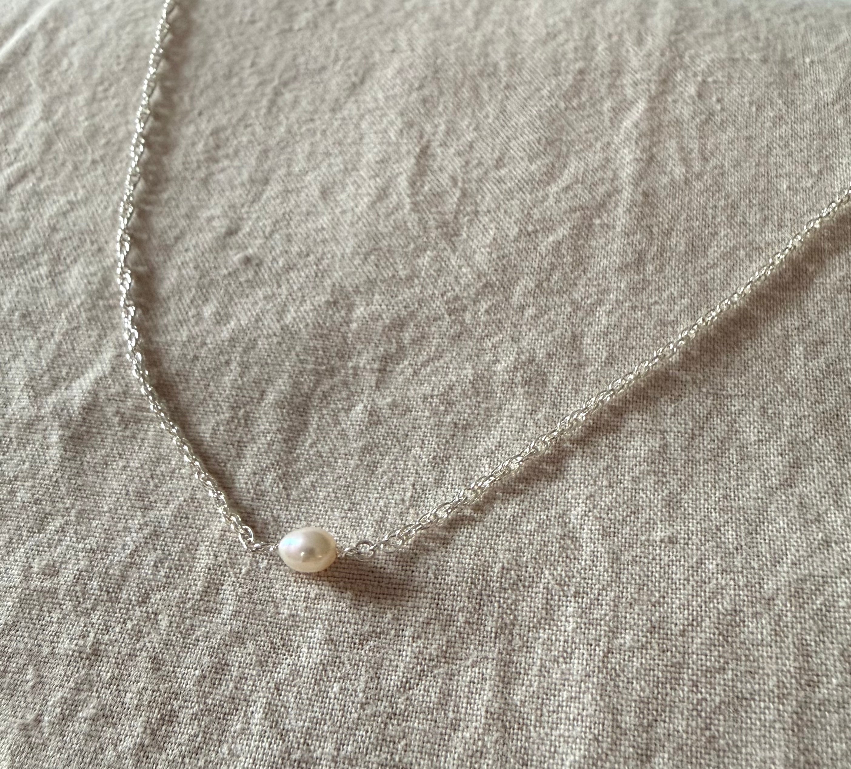 Silver Pearl necklace on a textured beige fabric background
