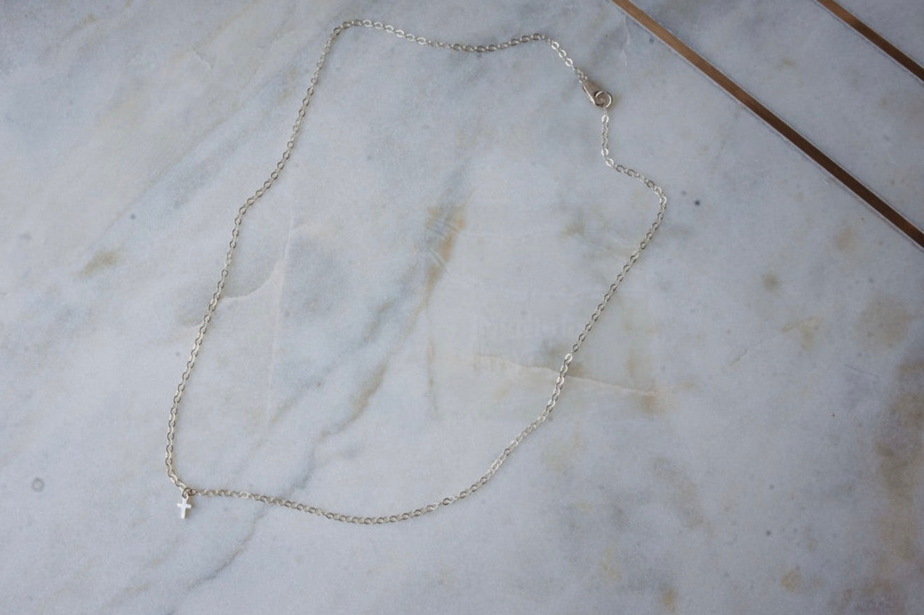 Silver chain necklace with small cross on a marble surface